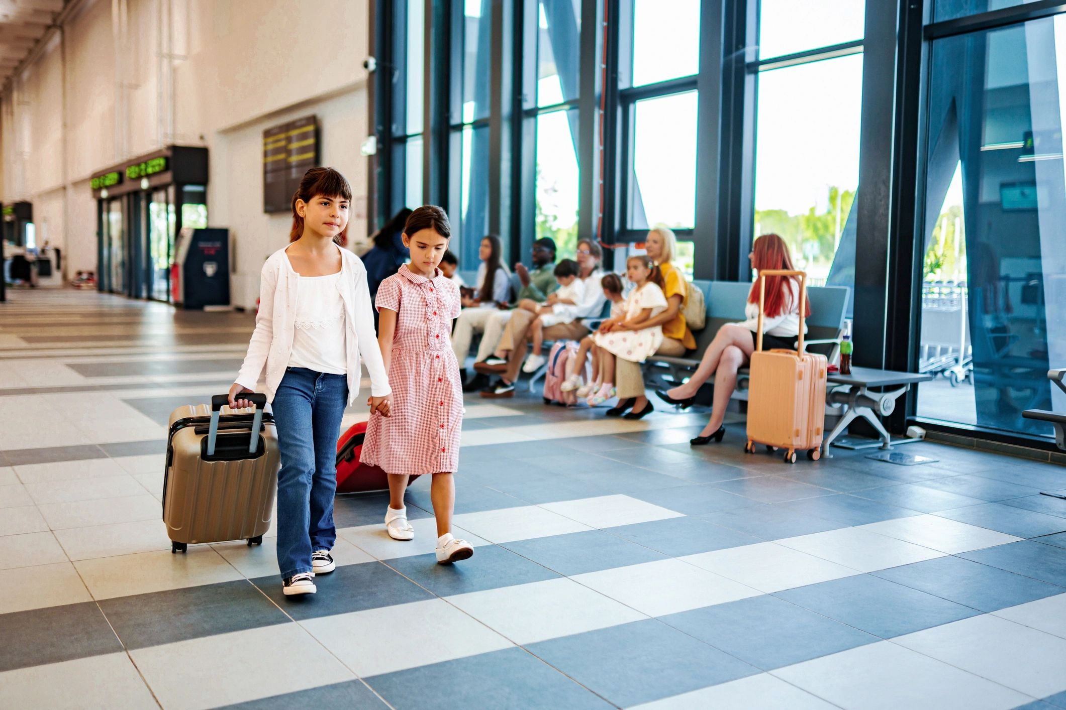 Two children walking through an airport terminal with suitcases